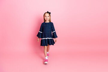 Charming young girl in a blue dress with cheerful pose against pink background showcasing casual...