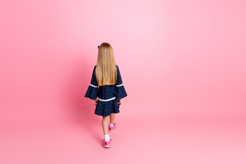 Young girl with long blonde hair in casual fashionable dress standing on pink background creating a...