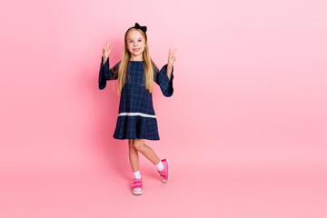 Young cheerful girl posing on a pink background wearing a fashionable dress and making peace...