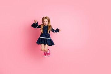 Cheerful young girl in fashionable attire jumping against a vibrant pink background, expressing...