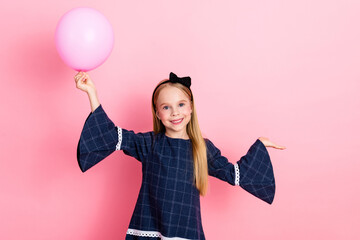 Smiling young girl holding a pink balloon, standing against a bright pastel backdrop, celebrating...