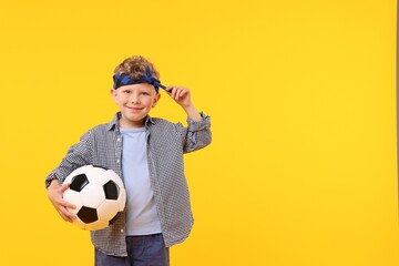 Little boy with soccer ball on yellow background, space for text