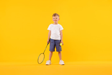 Little boy with racket and tennis ball on yellow background