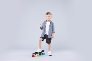 Little boy with penny board showing thumbs up on gray background