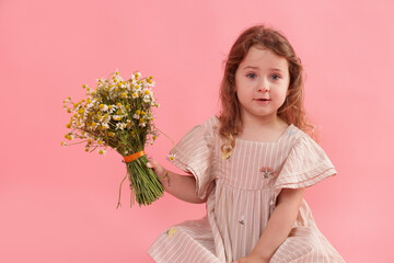 Cute little girl with bouquet of beautiful chamomile flowers on pink background