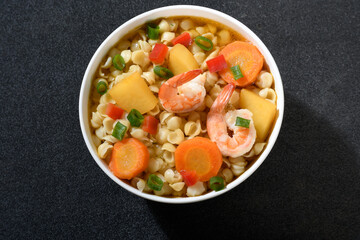 Shrimp and vegetable soup with shell pasta, white bowl on black background