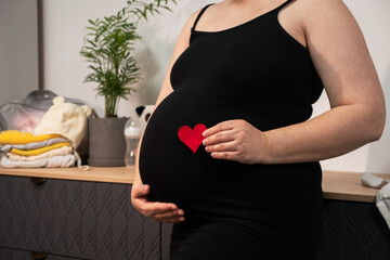 Pregnant woman holding red heart shape and feel love for unborn baby in belly. Awaiting for baby. Concept of maternity and pregnancy care