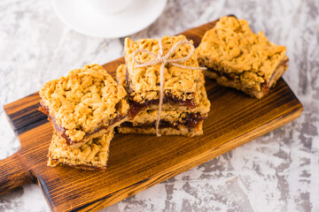 Delicious homemade pie with apple jam. Appetizing slices of grated pie with jam on a wooden board and coffee in a white cup on a light table.