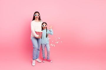 Happy mother and daughter enjoying popcorn and 3D movie experience on a vibrant pink background...