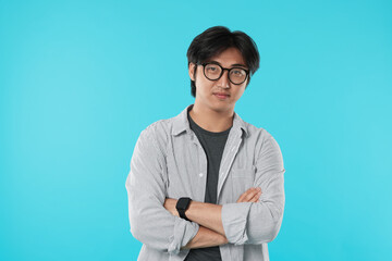 Handsome Asian man in glasses with crossed arms on light blue background