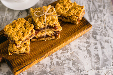 Delicious homemade pie with apple jam. Appetizing slices of grated pie with jam on a wooden board and coffee in a white cup on a light table.