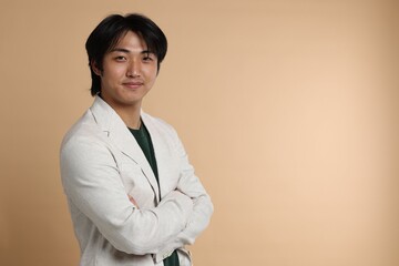 Portrait of handsome Asian businessman in suit with crossed arms on beige background. Space for text
