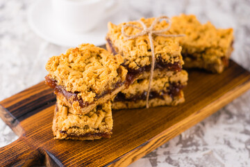 Delicious homemade pie with apple jam. Appetizing slices of grated pie with jam on a wooden board and coffee in a white cup on a light table.