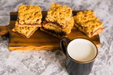 Delicious homemade pie with apple jam. Appetizing slices of grated pie with jam on a wooden board and a cup of milk on a light table.