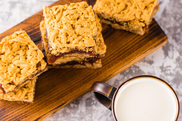 Delicious homemade pie with apple jam. Appetizing slices of grated pie with jam on a wooden board and a cup of milk on a light table.