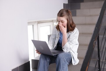 Cyber bullying. Upset teenage girl with laptop on stairs indoors