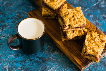 Delicious homemade pie with apple jam. Appetizing slices of grated pie with jam on a wooden board and a cup of milk on the table.