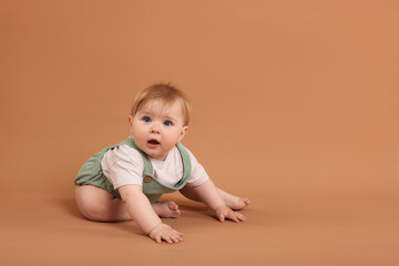 Cute little baby crawling on pale brown background, space for text
