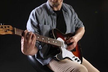 Man playing guitar on black background, closeup