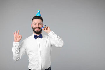 Happy Birthday. Handsome man with party hat and blower showing ok gesture on grey background, space...