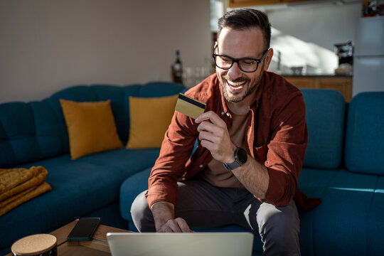 Happy man using laptop and credit card for online shopping at home