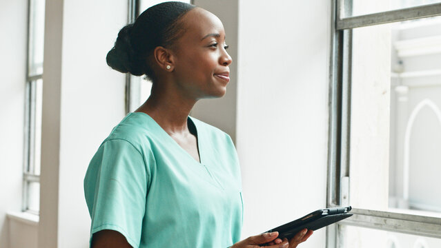 Healthcare Professional in Uniform Smiling Near Window with a Tablet