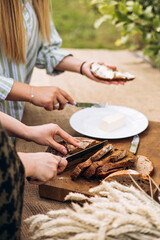 Female hands slicing fresh bread and spreading butter at outdoor garden picnic.