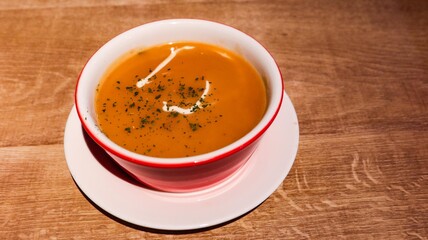 close up of a pumpkin soup on a wooden table with a touch of cream and herbs on top with copy space
