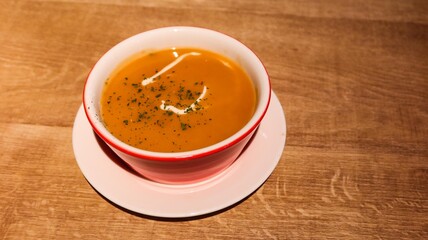 close up of a pumpkin soup on a wooden table with a touch of cream and herbs on top with copy space