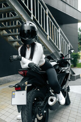 Sports girl in helmet poses sitting on a motorcycle in city. 
