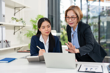 Fototapeta premium Focused female intern listening to senior business woman mentor teacher explaining online strategy looking at laptop computer teach trainee training new worker learning new skill at workplace.
