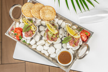 Gourmet seafood appetizers with diced tuna, avocado, lemon wedges, and microgreens served in oyster shells on white pebbles with toasted bread and sauce