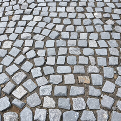 Patterned cobblestone pavement made of gray square stones laid in irregular gaps