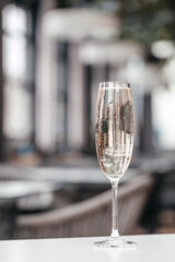 A tall glass of sparkling champagne stands on a sleek white table with a soft-focused modern interior in the background