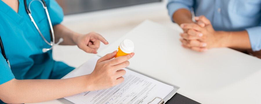 Doctor, female pharmacist holding a medicine bottle, gives advice, recommends how to take medicine to  patient. Explaining prescriptions, medical system concepts and health care.