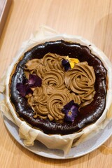 vertical photo of close up of freshly homebaked basque cheesecake with earl grey tea cream as topping and flower as decoration wrapped by a paper