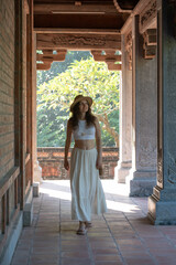Young woman with straw hat and white dress visiting Temple of Literature in Hanoi, Vietnam, ancient...