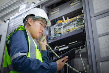 Network technician wearing safety helmet and vest performs LAN patchpanel inspection while holding...