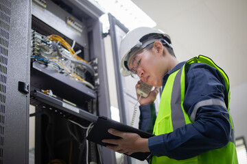 Network technician wearing safety helmet and reflective vest performs LAN patchpanel inspection...
