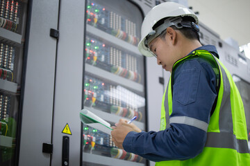 Engineer wearing safety helmet and reflective vest performs substation inspection to ensure...