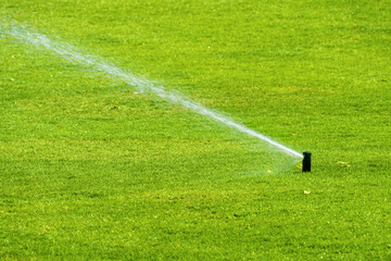 automatic lawn watering in summer in hot weather. Water splashes on the green grass in both...