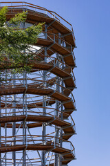 Modern wooden observation tower with spiral walkway against clear blue sky on a sunny day. Outdoor...