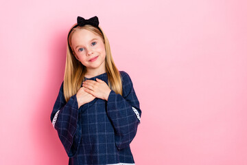 Young girl in casual plaid outfit with heart gesture against pink background, expressing kindness...
