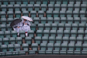 Two people sit alone with umbrellas in seats at Wimbledon Centre Court after covers go on when rain...