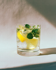 Close-up of a refreshing glass of sparkling water with lemon and mint on a sunny table