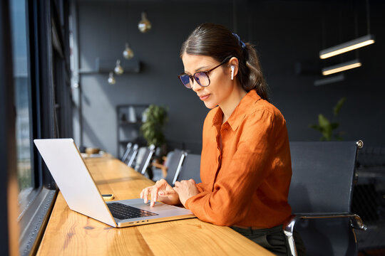 Indian entrepreneur manager businesswoman using pc for communication, learning at workplace. Focused latin hispanic young business woman working on laptop computer sitting at office workplace desk