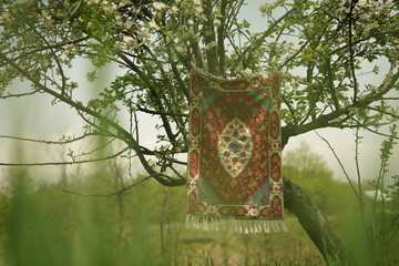 A Kaar Kash handmade Kashmiri carpet hung under a blossoming spring tree &mdash; a timeless blend of craftsmanship and nature rooted in tradition.
