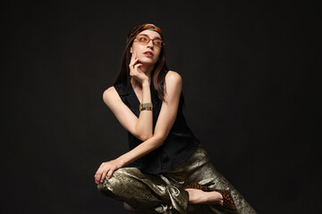 Beautiful woman in stylish outfit sitting on chair against black background