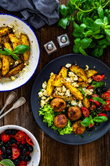 Greek style fried meatballs, fried potato wedges with feta cheese and tomato salad on wooden table	
