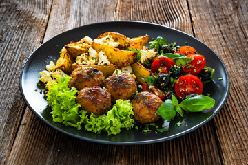 Greek style fried meatballs, fried potato wedges with feta cheese and tomato salad on wooden table	